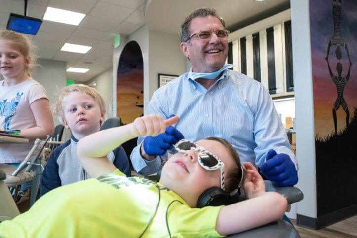 Pediatric dentist in Centerville smiling with three young patients data-lazy-srcset=